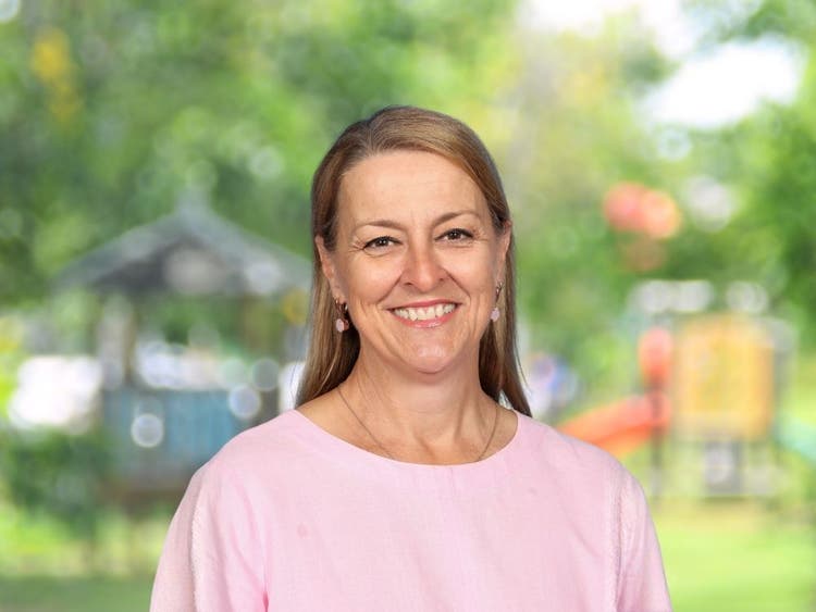 Sue Roach wearing pink top in front of blurred school playground