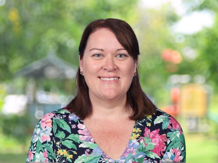 Claire Pellegrini wearing black and coloured floral top in front of blurred school playground