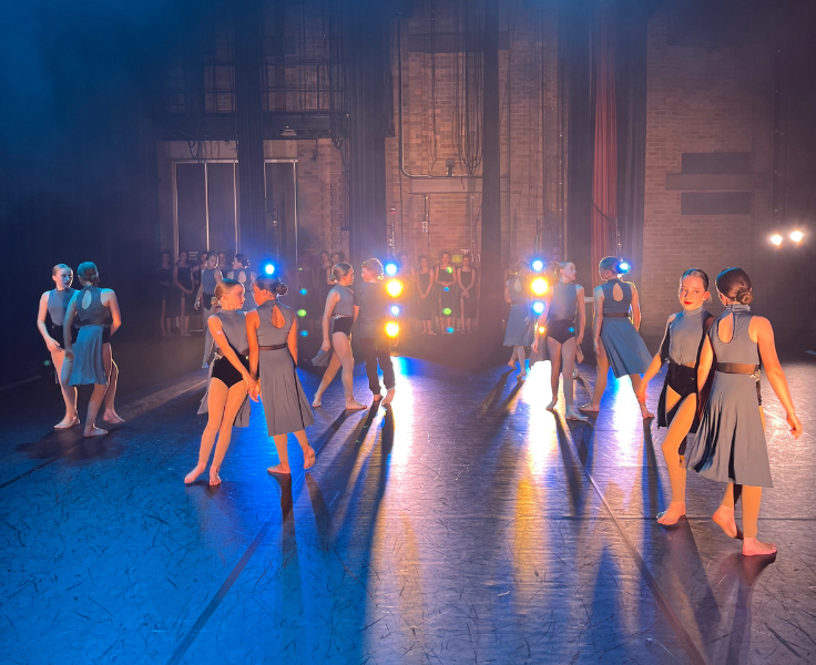 Dancers wearing blue dresses on stage with blue and yellow moody lighting
