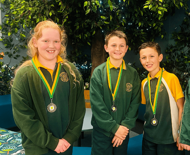 Three students in green and gold uniform wearing medllions around their necks
