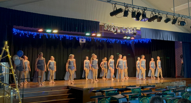 Girls wearing purple dance costumes standing on stage under blue lights